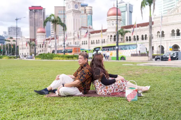 50 'li yaşlarda Malezyalı bir adam ve 30' lu yaşlarda Çinli bir kadın. İkisi de Malezya 'nın başkenti Kuala Lumpur' da bulunan tarihi bir binanın önündeki çimlerin üzerinde oturuyorlar..