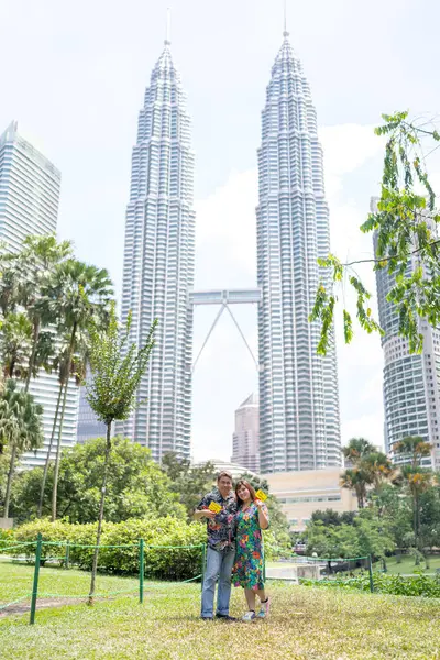 50 'li yaşlarda açık mavi tişört giyen Malezyalı bir adam ve 30' lu yaşlarında Çinli bir kadın Kuala Lumpur, Malezya 'da KLCC Park' ta gökdelenler eşliğinde evlenme teklif ediyor..