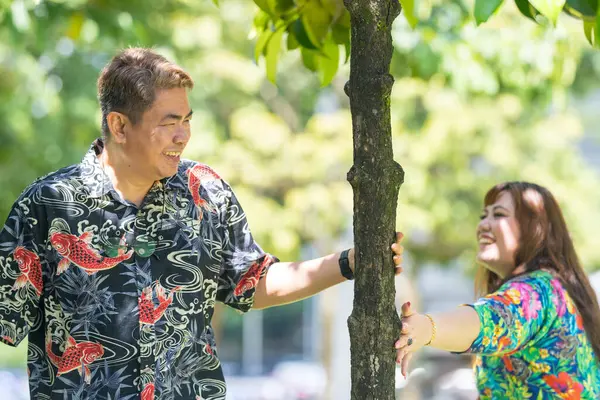 50 'li yaşlarında Malezyalı bir adam renkli gömlek giyiyor ve 30' lu yaşlarında Çinli bir kadın Malezya, Kuala Lumpur 'daki KLCC Parkı' nda ağaçların gölgesinde kovalamaca oynuyor..