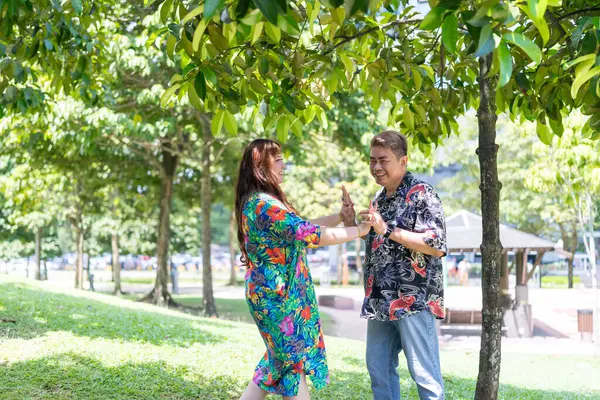 50 'li yaşlarında Malezyalı bir adam renkli gömlek giyiyor ve 30' lu yaşlarında Çinli bir kadın Malezya, Kuala Lumpur 'daki KLCC Parkı' nda ağaçların gölgesinde kovalamaca oynuyor..