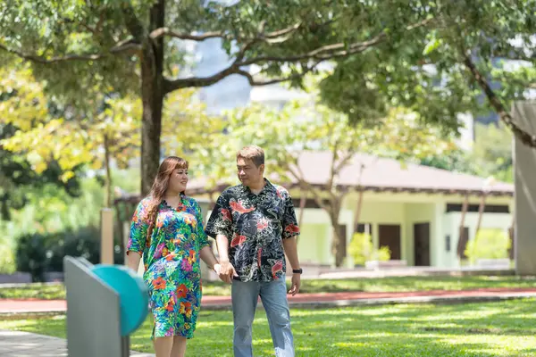 50 'li yaşlarda Malezyalı bir adam renkli gömlek giyiyor ve 30' lu yaşlarında Çinli bir kadın Malezya 'nın Kuala Lumpur kentindeki KLCC Parkı' nda birlikte yürüyor..