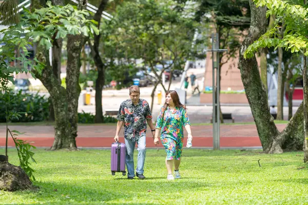 50 'li yaşlarda Malezyalı bir adam renkli gömlek giyiyor ve 30' lu yaşlarında Çinli bir kadın Malezya 'nın Kuala Lumpur kentindeki KLCC Parkı' nda birlikte yürüyor..