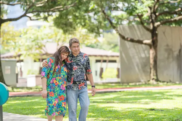 50 'li yaşlarda Malezyalı bir adam renkli gömlek giyiyor ve 30' lu yaşlarında Çinli bir kadın Malezya 'nın Kuala Lumpur kentindeki KLCC Parkı' nda birlikte yürüyor..