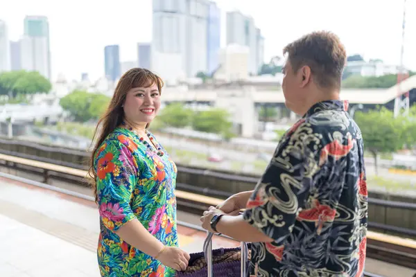50 'li yaşlarında Malezyalı bir adam renkli gömlek giyiyor ve 30' lu yaşlarında Çinli bir kadın renkli elbiseler giyiyor. Kuala Lumpur, Malezya 'da bir tren istasyonunda birlikte vakit geçiriyorlar..