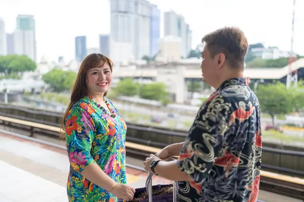 50 'li yaşlarında Malezyalı bir adam renkli gömlek giyiyor ve 30' lu yaşlarında Çinli bir kadın renkli elbiseler giyiyor. Kuala Lumpur, Malezya 'da bir tren istasyonunda birlikte vakit geçiriyorlar..