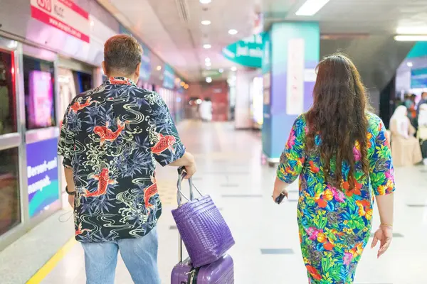 stock image Malay man in his 50s wearing colorful shirt and Chinese woman in her 30s wearing colorful dress, walking through a subway station in Kuala Lumpur, Malaysia.