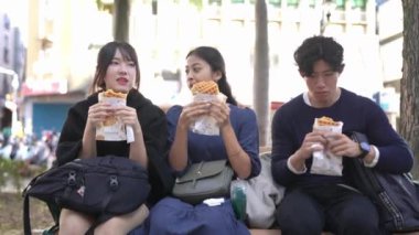 Tayvanlı 20 'li yaşlarda erkek ve bayan öğrenciler ve Tayvan' ın Tayvan şehrindeki Daan Bölgesi 'nde bir üniversitenin yanındaki bankta oturan Güney Asyalı bir kız öğrenci waffle' ların keyfini çıkarıyorlar. Yavaş çekim