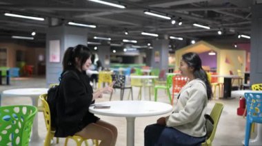 Yavaş çekimde, Taipei 'nin Da' an Bölgesi 'ndeki bir üniversite kafeteryasında otururken, biri Tayvanlı, biri Güney Asyalı iki genç kadını dostça sohbet ederken görüntülüyor..