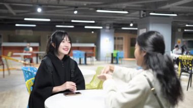 Yavaş çekimde, Taipei 'nin Da' an Bölgesi 'ndeki bir üniversite kafeteryasında otururken, biri Tayvanlı, biri Güney Asyalı iki genç kadını dostça sohbet ederken görüntülüyor..