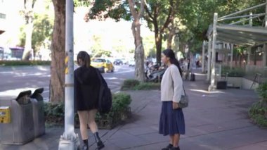 Tayvanlı genç bir kadın ve Güney Asyalı bir kadının, Taipei 'nin Da' an Bölgesi 'ndeki bir üniversite yakınlarında halka açık bir yolda yürüyüş ve sohbetlerini gösteren yavaş çekim bir video..