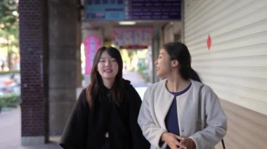 Tayvanlı genç bir kadın ve Güney Asyalı bir kadının, Taipei 'nin Da' an Bölgesi 'ndeki bir üniversite yakınlarında halka açık bir yolda yürüyüş ve sohbetlerini gösteren yavaş çekim bir video..
