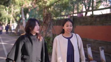 Tayvanlı genç bir kadın ve Güney Asyalı bir kadının, Taipei 'nin Da' an Bölgesi 'ndeki bir üniversite yakınlarında halka açık bir yolda yürüyüş ve sohbetlerini gösteren yavaş çekim bir video..