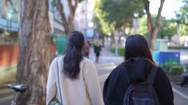 Tayvanlı genç bir kadın ve Güney Asyalı bir kadının, Taipei 'nin Da' an Bölgesi 'ndeki bir üniversite yakınlarında halka açık bir yolda yürüyüş ve sohbetlerini gösteren yavaş çekim bir video..