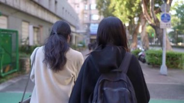 Tayvanlı genç bir kadın ve Güney Asyalı bir kadının, Taipei 'nin Da' an Bölgesi 'ndeki bir üniversite yakınlarında halka açık bir yolda yürüyüş ve sohbetlerini gösteren yavaş çekim bir video..