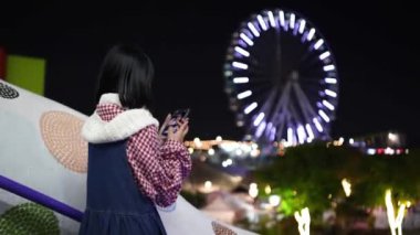 Tayvan 'ın Shilin bölgesinde, Tayvanlı bir kadın, yirmili yaşlarda, gece vakti Tayvan' daki lunaparkta akıllı telefondan Ferris tekerleğini yakalıyor..