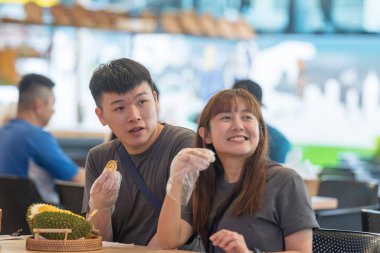 30 'lu yaşlarda Çinli Malezyalı bir çift Kuala Lumpur, Malezya' da turistler arasında popüler olan ünlü bir dükkanda Durian yerken sohbet ediyorlar..