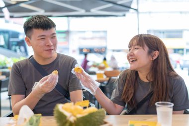 30 'lu yaşlarda Çinli Malezyalı bir çift Kuala Lumpur, Malezya' da turistler arasında popüler olan ünlü bir dükkanda Durian yerken sohbet ediyorlar..