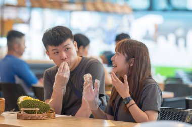 30 'lu yaşlarda Çinli Malezyalı bir çift Kuala Lumpur, Malezya' da turistler arasında popüler olan ünlü bir dükkanda Durian yerken sohbet ediyorlar..