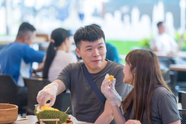 30 'lu yaşlarda Çinli Malezyalı bir çift Kuala Lumpur, Malezya' da turistler arasında popüler olan ünlü bir dükkanda Durian yerken sohbet ediyorlar..