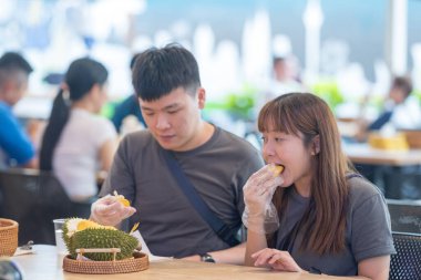 30 'lu yaşlarda Çinli Malezyalı bir çift Kuala Lumpur, Malezya' da turistler arasında popüler olan ünlü bir dükkanda Durian yerken sohbet ediyorlar..