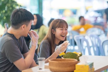 30 'lu yaşlarda Çinli Malezyalı bir çift Kuala Lumpur, Malezya' da turistler arasında popüler olan ünlü bir dükkanda Durian yerken sohbet ediyorlar..