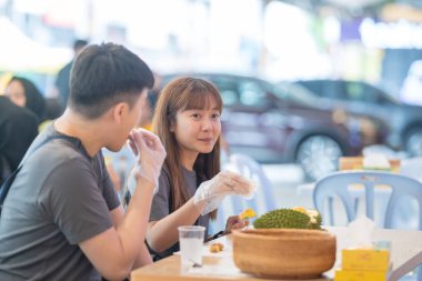 30 'lu yaşlarda Çinli Malezyalı bir çift Kuala Lumpur, Malezya' da turistler arasında popüler olan ünlü bir dükkanda Durian yerken sohbet ediyorlar..