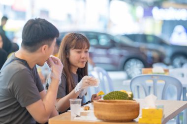 30 'lu yaşlarda Çinli Malezyalı bir çift Kuala Lumpur, Malezya' da turistler arasında popüler olan ünlü bir dükkanda Durian yerken sohbet ediyorlar..