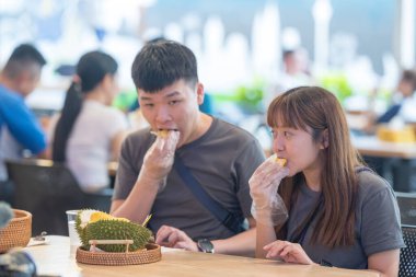 30 'lu yaşlarda Çinli Malezyalı bir çift Kuala Lumpur, Malezya' da turistler arasında popüler olan ünlü bir dükkanda Durian yerken sohbet ediyorlar..