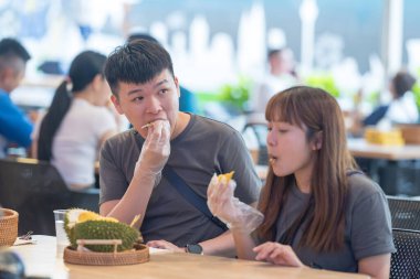 30 'lu yaşlarda Çinli Malezyalı bir çift Kuala Lumpur, Malezya' da turistler arasında popüler olan ünlü bir dükkanda Durian yerken sohbet ediyorlar..