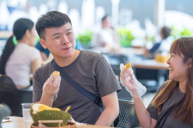 30 'lu yaşlarda Çinli Malezyalı bir çift Kuala Lumpur, Malezya' da turistler arasında popüler olan ünlü bir dükkanda Durian yerken sohbet ediyorlar..