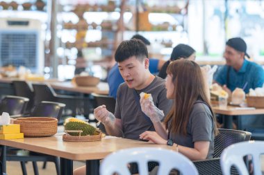 30 'lu yaşlarda Çinli Malezyalı bir çift Kuala Lumpur, Malezya' da turistler arasında popüler olan ünlü bir dükkanda Durian yerken sohbet ediyorlar..