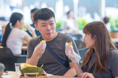 30 'lu yaşlarda Çinli Malezyalı bir çift Kuala Lumpur, Malezya' da turistler arasında popüler olan ünlü bir dükkanda Durian yerken sohbet ediyorlar..