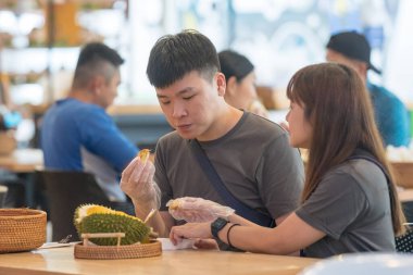30 'lu yaşlarda Çinli Malezyalı bir çift Kuala Lumpur, Malezya' da turistler arasında popüler olan ünlü bir dükkanda Durian yerken sohbet ediyorlar..