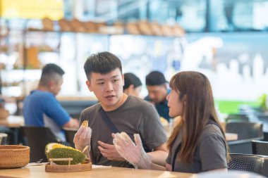 30 'lu yaşlarda Çinli Malezyalı bir çift Kuala Lumpur, Malezya' da turistler arasında popüler olan ünlü bir dükkanda Durian yerken sohbet ediyorlar..