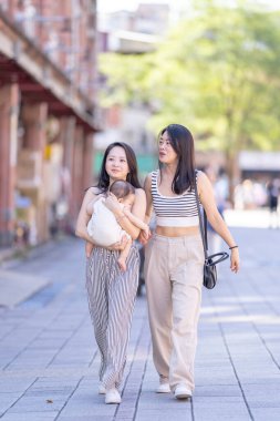 30 'lu yaşlarda Tayvan' ın Taipei şehrinde Dihua Caddesi boyunca yürüyen sıradan kıyafetler giyen iki Tayvanlı kadın, her biri 6 aylık bir bebek taşıyor..