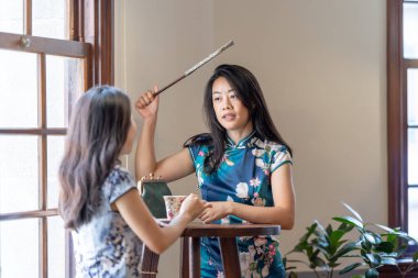 Two Taiwanese women in their 30s wearing traditional Chinese clothing chat at a table by the window of a traditional building on Dihua Street in Taipei City, Taiwan, in September. clipart