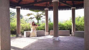 20 'li yaşlarda, sarı elbiseli Çinli bir kadın Malezya' nın Kuala Lumpur yakınlarındaki Bukit Jalil 'deki büyük doğa dolu bir parkın ormanına bakıyor. (Ağır çekim video)