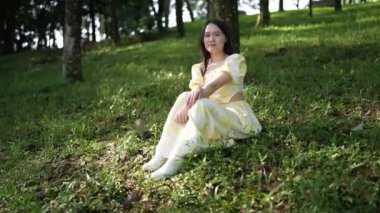 20 'li yaşlarda, sarı elbiseli Çinli bir kadın Malezya' nın Kuala Lumpur yakınlarındaki Bukit Jalil 'deki büyük doğa dolu bir parkın ormanına bakıyor. (Ağır çekim video)