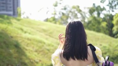 20 'li yaşlarda, sarı elbiseli Çinli bir kadın Malezya' nın Kuala Lumpur yakınlarındaki Bukit Jalil 'deki büyük doğa dolu bir parkın ormanına bakıyor. (Ağır çekim video)