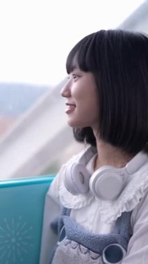 20 'li yaşlarında Tayvanlı genç bir kadın Tayvan' ın Taipei şehrindeki Shilin semtinde bir lunaparkta fotoğraf çekiyor ve müzik dinliyor. Dikey video.