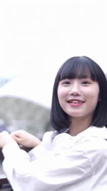 20 'li yaşlarında Tayvanlı genç bir kadın Tayvan' ın Taipei şehrindeki Shilin semtindeki lunaparkta fotoğraf çekiyor ve müzik dinliyor. Dikey yavaş çekim videosu.