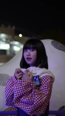Tayvan 'ın Taipei şehrindeki Shilin semtinde bir lunaparkta buluşurken 20' li yaşlarda genç bir Tayvanlı kadın geceleri merdivenlerde vakit geçiriyor. Dikey yavaş çekim videosu.