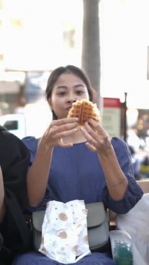 Tayvanlı 20 'li yaşlarda erkek ve bayan öğrenciler ve Tayvan' ın Taipei şehrinde halka açık bir yolda waffle yiyip sohbet eden Hintli bir kadın. Dikey.