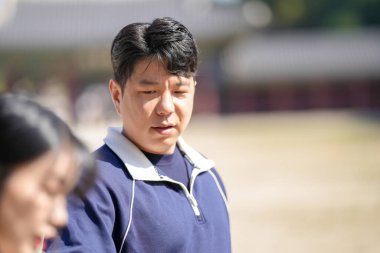 A sporty Korean couple, a man in his 30s and a woman in her 20s, wearing tracksuits, spends their time together happily at a historical building in Seoul, South Korea. clipart