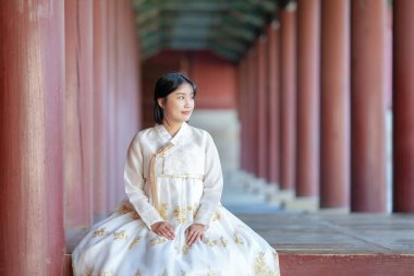 A Korean woman in her 20s wearing a white hanbok sits dignifiedly in a historical building in Seoul, South Korea. clipart