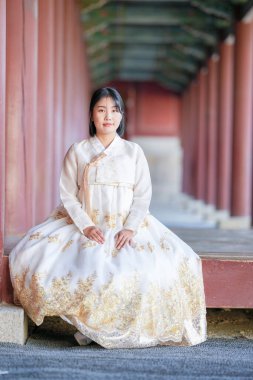 A Korean woman in her 20s wearing a white hanbok sits dignifiedly in a historical building in Seoul, South Korea. clipart