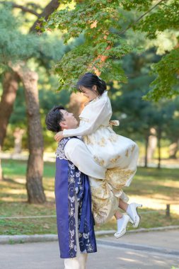 Koreli bir çift, 30 'lu yaşlarda bir adam ve 20' li yaşlarında bir kadın, Güney Kore, Seul 'de yeşil ağaçlarla çevrili bir parkta Hanbok giyip birbirlerine sarılıyorlar..