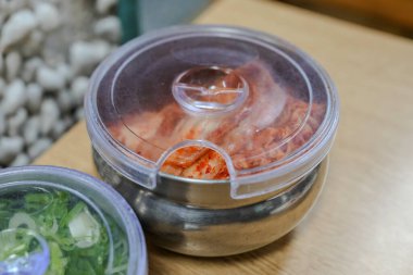 Tepesinde kapağı olan bir kase yemek. Kapağı açık ve sapı var. Kase ahşap bir masanın üzerinde.