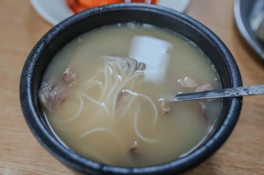 İçinde erişte ve et olan bir kase çorba. Kasede bir kaşık var.