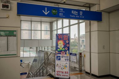 Yukarıya bakan mavi bir okla imzala. İşaret yabancı bir dilde. Duvarda bir kişinin resminin olduğu bir poster var.